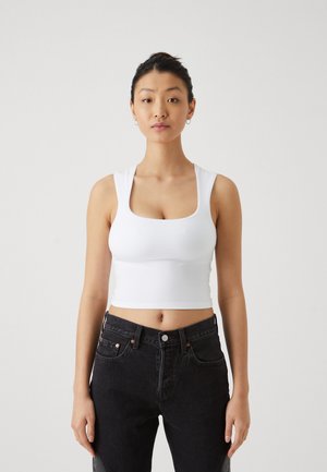 Weißes, kurzes Tanktop aus dehnbarem Stoff mit quadratischem Ausschnitt und breiten Trägern, kombiniert mit hochgeschnittenen schwarzen Jeans.