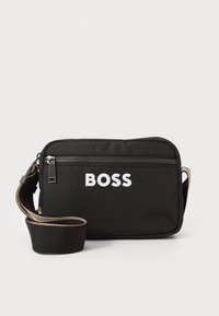 Musta suorakaiteenmuotoinen laukku tekstiilimateriaalista. Siinä on etutasku vetoketjulla, jossa on "BOSS"-merkintä valkoisin, paksuin kirjaimin, sekä säädettävä olkahihna.