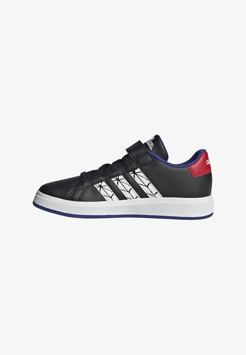 Chaussures de sport noires avec un design à trois bandes blanches, une bride velcro et un accent rouge au niveau du talon. Semelle en caoutchouc avec un contour bleu. Texture lisse.