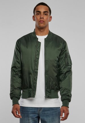 Green satin bomber jacket with ribbed cuffs and hem, featuring a front zipper and side pockets. Worn over a white t-shirt and blue jeans.