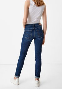 Tmavě modré džíny slim fit s ohrnutými nohavicemi, které mají dvě zadní kapsy a hnědou koženou nášivku na pase.