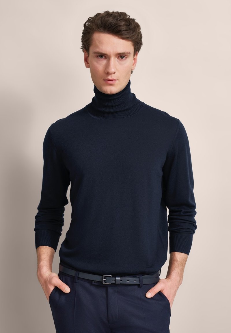 Navyfarbener Rollkragenpullover aus glattem Strickstoff. Enganliegende Silhouette mit langen Ärmeln und gerippten Bündchen, kombiniert mit dunklen Hosen und einem Gürtel.
