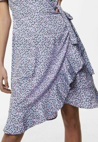 Lila Blumen-Wickelkleid mit gerüschtem Saum, das ein kleines abstraktes Muster in Schwarz und Türkis aufweist. Hergestellt aus leichtem Stoff mit weicher Textur.