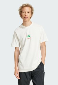Witte katoenen t-shirt met een klein groen en rood logo op de borst. Korte mouwen en een reguliere pasvorm. Glad texture, casual ontwerp.