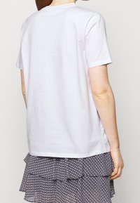 Bílé tričko s krátkým rukávem a kulatým výstřihem, vyrobené z měkké bavlny, spárované s vrstvenou sukní s černobílým vzorem.