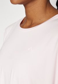 Light pink athletic shirt featuring a round neckline and short sleeves, with a subtle logo detail in a slightly darker shade. Smooth fabric texture.