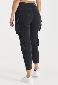 Pantalones cargo negros con bolsillos laterales, una cintura ajustada y un diseño de pierna tapered. La tela tiene un acabado texturizado. Combinados con zapatillas blancas.
