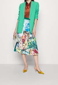 Blazer verde, top in satin marrone, gonna midi con stampa acquerello, mules gialle con punta, borsa verde chiaro.