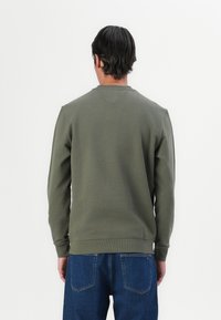 Olivengrøn sweatshirt med rund hals, der har ribbede manchetter og bund, samt en V-syning detalje på ryggen. Sammen med blå denimbukser.