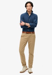 Lange mouwen blauwe linnen shirt met een button-down kraag, gecombineerd met beige chinos en crèmekleurige sneakers met bruine accenten. Bruin leren riem.