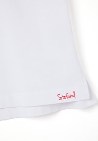 Top bianco leggero con una texture liscia; presenta un logo ricamato "Stefanel" rosso all'orlo. Design semplice, maniche corte.