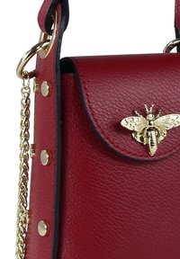 Sac à main en cuir rouge avec une finition texturée, comprenant un fermoir abeille doré, une bandoulière chaîne en or et des accents cloutés sur le côté.