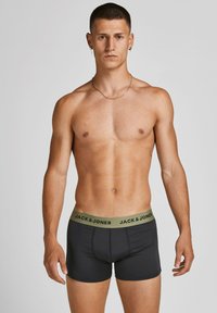 Schwarze Boxershorts mit einem grünen elastischen Bündchen, das den Markennamen "JACK & JONES" in fettem schwarzen Text zeigt. Stretchstoffdesign.