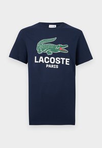 Μπλε ναυτικό T-shirt με λογότυπο πράσινου κροκόδειλου και λευκό κείμενο «LACOSTE PARIS» στο μπροστινό μέρος, κοντά μανίκια, στρογγυλή λαιμόκοψη.
