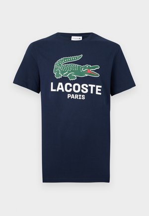 Tmavě modré tričko s krátkými rukávy, kulatým výstřihem, zeleným krokodýlím logem a bílým nápisem "LACOSTE PARIS" na přední straně.