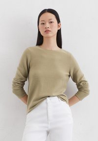 Olive green knit sweater with a crew neck and long sleeves, paired with high-waisted white jeans. Smooth texture, casual fit.