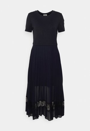 Schwarzes Kleid mit einem enganliegenden Oberteil mit kurzen Ärmeln und einem fließenden, gefältelten, transparenten Rock. Ein detaillierter Spitzenbesatz am Saum sorgt für Textur und visuelles Interesse.