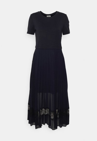 Vestido negro que presenta un top ajustado de mangas cortas y una falda fluida y plisada de tela transparente. Un delicado borde de encaje en el dobladillo añade textura e interés visual.