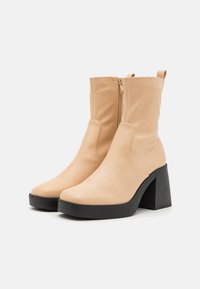 Beige leather ankle boots with a rounded toe, side zipper, and a chunky black heel. Smooth texture with subtle stitching details.