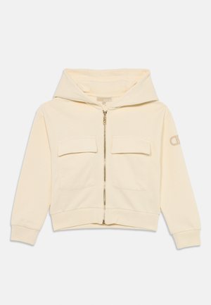 Cream-colored hoodie with a front zipper, two chest pockets, and ribbed cuffs. Features a logo on the sleeve and a soft, smooth texture.