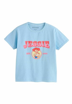 Világoskék póló piros "JESSIE" felirattal, egy rajzfilmfigura egy sárga körben alul, és "EST. 1999" felirat mindkét oldalon.