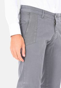 Pantaloni grigi in cotone con tasche laterali, chiusura con zip e una texture liscia, abbinati a una camicia bianca a maniche lunghe.