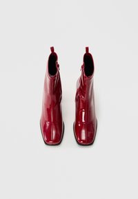 Bottines noires en vernis avec un bout pointu, design angulaire et fermeture éclair, présentant une finition brillante et une texture lisse.