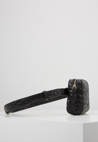 Borsa in pelle nera con stampa coccodrillo, di forma rettangolare, dotata di chiusura con zip e tracolla regolabile. Dettaglio di superficie texture.