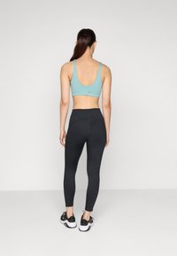 Soutien-gorge de sport bleu clair avec de larges bretelles et un dos en scoop, associé à un legging noir taille haute et des chaussures de sport noires avec des semelles blanches.