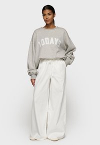 Felpa grigia con la scritta "10 DAYS" in bianco, abbinata a pantaloni bianchi a vita alta e larghi e scarpe beige senza lacci.