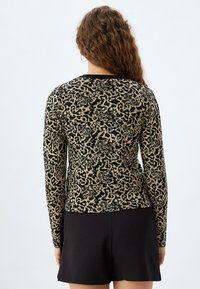 Maglione a maniche lunghe con stampa astratta nera e beige, texture lavorata a maglia e scollo nero. Abbinato a una gonna nera.
