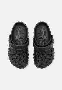 Une paire de sabots Crocs noirs avec une surface texturée géométrique et des trous de ventilation, dotés de sangles arrière ajustables, vus de dessus.