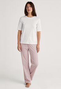 Vit t-shirt med kort ärm, kombinerad med rosa randiga byxor med marinblå linjer. Tyget verkar mjukt med en avslappnad passform.