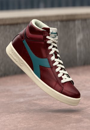 High-top sneaker in burgundy leather with teal accents, white laces, and a textured cream rubber sole. Features logo on the tongue.
