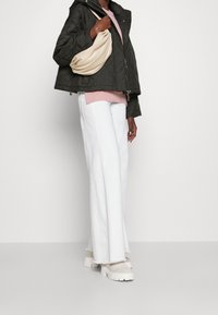 Giacca nera trapuntata, maglione rosa chiaro, jeans bianchi a gamba larga e borsa a tracolla beige; la modella indossa scarpe beige voluminose.