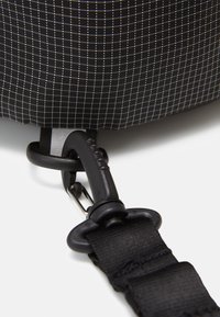 Black fabric bag featuring a grid pattern, durable material, with a black clip and adjustable strap attached at the bottom.
