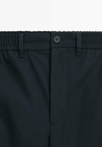 Dark navy pants waistband with elastic back, belt loops, and a single black button closure at front center.