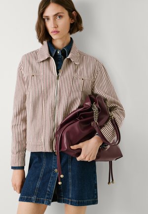 Gestreepte spijkerjacket met licht- en donkerrode lijnen, gecombineerd met een donkere spijkerrok. Houdt een bordeauxrode leren tas met kettingaccenten vast.