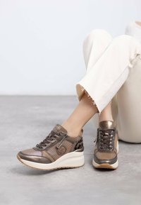 Brown leather and textile sneakers with decorative stitching, a lace-up front, and textured accents. The sole is chunky and white.