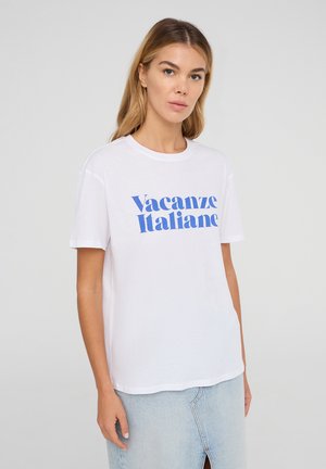 T-shirt in cotone bianco con una tipografia blu che recita "Vacanze Italiane." Le maniche corte e il collo a giro completano il design casual.