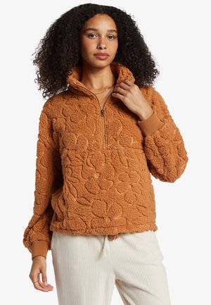Faux fur trøje i orange med blomstertekstur, halvdækkende lynlås ved halsen og ribbede manchetter. Snørelukning i kanten til justerbar pasform.