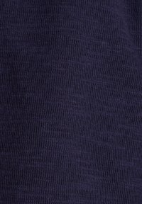 Närbild av mörkblå ribbad stickad tyg med vertikala texturerade linjer och subtila färgvariationer.