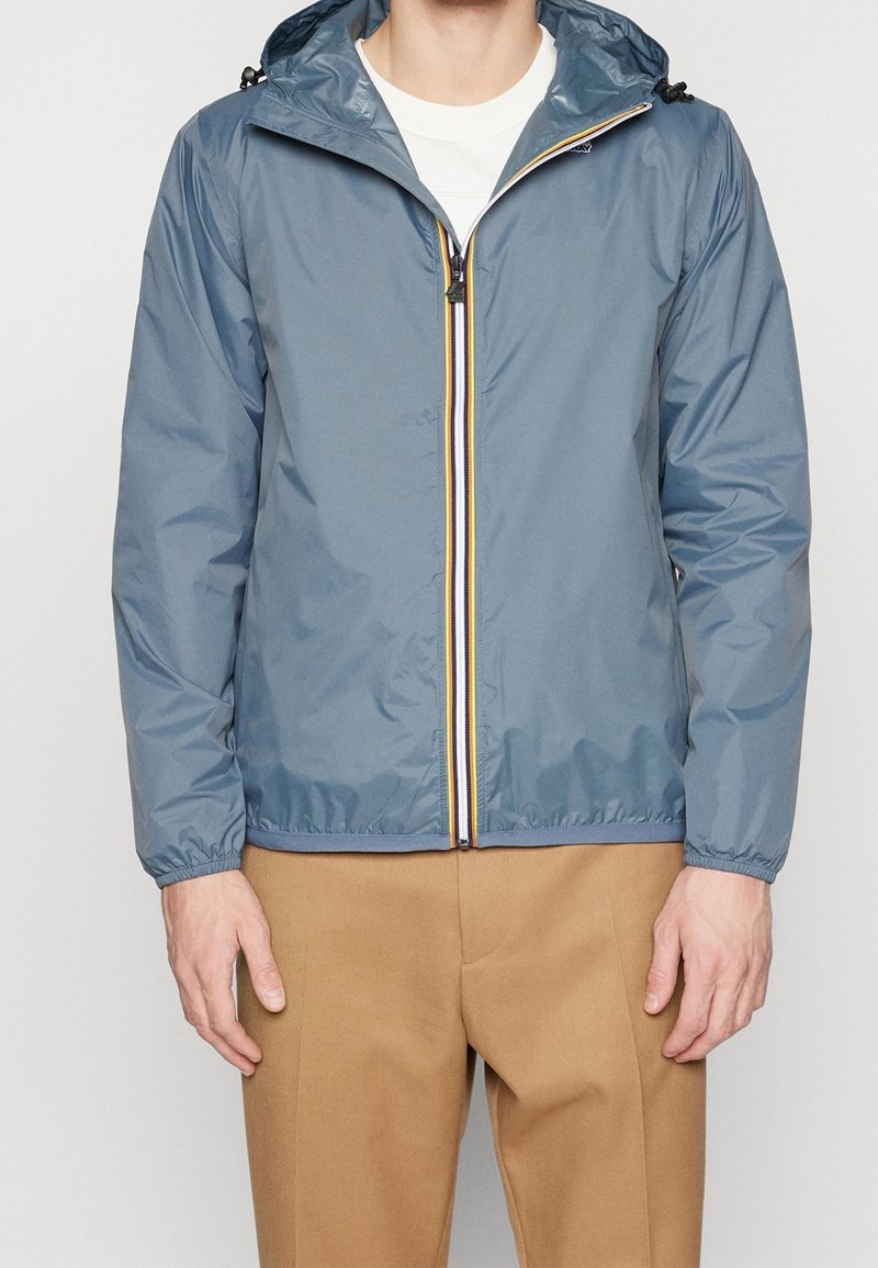 Leichte blaue Jacke mit verstellbarem Kapuzenzug, Reißverschluss vorne und einem mehrfarbigen Streifen sowie elastischen Bündchen. Glatte Textur, lässiges Design.