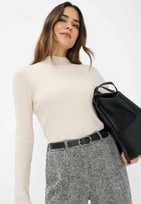 Lichtbeige geribde trui met hoge hals, gecombineerd met gestreepte grijze broek en een zwarte tote bag, met een gladde textuur en strakke ontwerp.