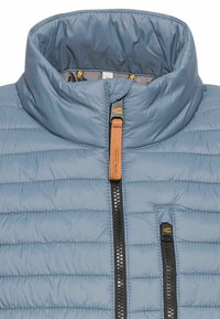 Light blue padded jacket with a high collar, featuring a central zipper and two zippered pockets, accented with brown faux leather pulls.