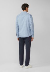 Jasnoniebieska koszula z długim rękawem, wzorzysta, z kołnierzykiem, zapinanymi mankietami i prostym dołem, w zestawie z ciemnymi spodniami i białymi tramkami.