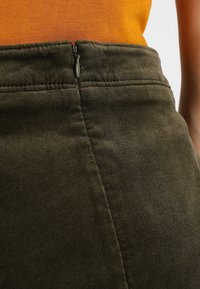 Khaki zielona spódnica z teksturowanym materiałem, z zamkiem błyskawicznym z tyłu. Pas jest dopasowany, z widocznymi akcentami szyć.