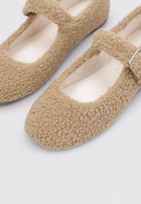 Brown fuzzy Mary Jane shoes with a textured upper, rounded toe, and a strap featuring a silver buckle. Soft inner lining for comfort.