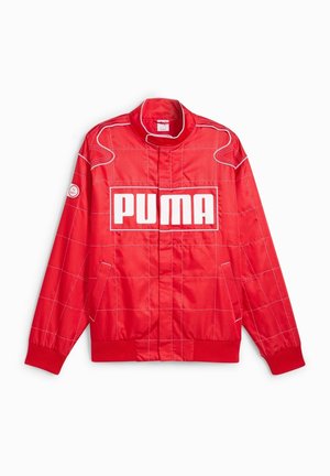 Veste Puma rouge avec des lignes blanches en quadrillage, des poignets et un ourlet côtelés, un col montant, des poches latérales et un grand logo Puma blanc sur la poitrine.