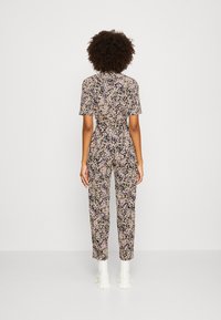 Combinaison florale avec des manches courtes, une taille cintrée et une jambe fuselée, sur un fond noir parsemé de petites fleurs roses, blanches et jaunes.